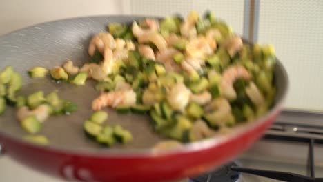 Female-hand-tossing-and-frying-shrimps-and-zucchini-in-a-pan