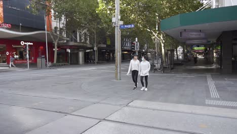 Girls-walk-through-empty-Melbourne-city-during-the-COVID-lockdown-as-coronavirus-restrictions-take-hold---Bourke-Street,-Melbourne,-Australia