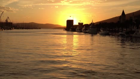 Tower-Kamerlengo-profiled-in-front-of-the-sun-at-sunset-with-shiny-gentle-waves-moving-in-the-foreground-in-the-town-of-Trogir-in-Croatia