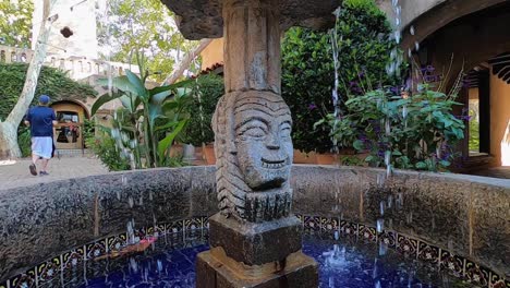 A-tourist-walks-past-a-fountain-in-one-of-the-many-courtyards-throughout-the-Tlaquepaque-Arts-and-Shopping-Village,-Sedona,-Arizona