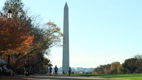 Pedestrians-walking-along-park-with-colorful-trees-during-sunny-day-and-the-Washington-Monument-in-the-background