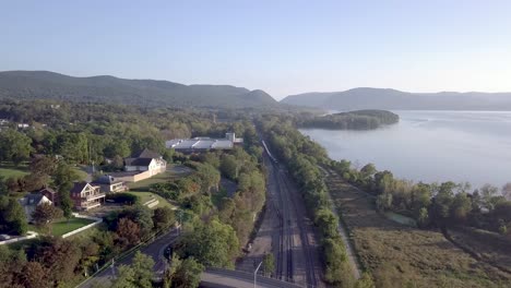 Aerial-footage-of-a-MetroNorth-train-arriving-in-Beacon,-New-York-in-the-Hudson-Valley-with-the-Hudson-River-in-the-background