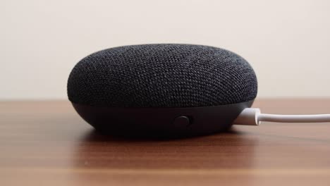 Person-pressing-a-Google-Nest-Home-Mini-smart-speaker-with-built-in-Google-Assistant-on-a-wooden-table