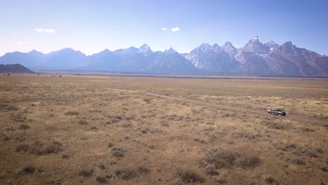 Drone-shot-of-the-Grand-Teton-National-Park-with-the-Tetons-visible-and-the-grasslands-brilliant-below