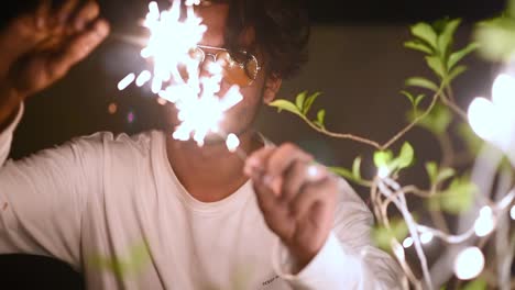 Cheerful-teenager-male-celebrates-Christmas,-Diwali-or-New-year-by-playing-with-fireworks-and-crackers-near-led-light-decorated-plant,-Slow-motion