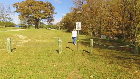 woman-walks-through-park-no-cars-beyond-this-point-sign-and-remains-on-park-trail