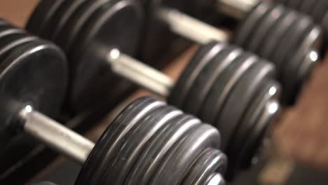 Closeup-slow-slider-shot-to-the-right-looking-down-at-severe-angle-on-row-of-dumbbells-on-a-rack-with-shallow-depth-of-field
