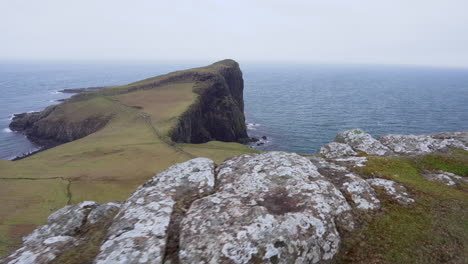 Tracking-shot-of-Neist-Point-lighthouse-with-rocky-cliffs-in-foreground-and-Atlantic-Ocean-in-the-background-on-a-windy-and-cloudy-day-in-Scotland,-Isle-of-Skye