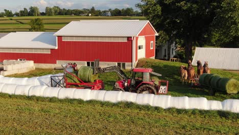 Steel-wheeled-Amish-tractor-places-round-hay-bale-on-wrapping-machine,-aerial