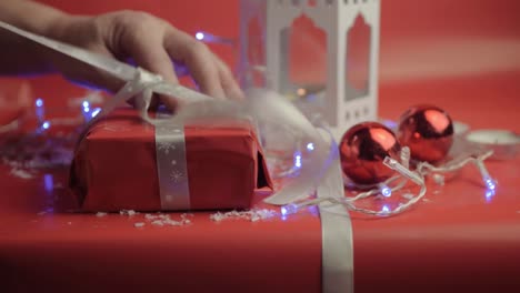 Weihnachtsgeschenk-Mit-Band-Und-Rotem-Papier-Mit-Rotem-Hintergrund-Und-Kugeln-Auspacken