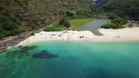 Drone-Shot-flying-towards-a-crowd-of-people-surrounding-a-Slip-n-Slide-on-the-beach-at-Waimea-Bay,-Hawaii