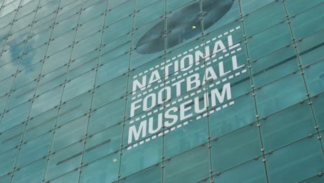 National-Football-Museum-sign-on-side-of-building-tourist-attraction-public-location-Greater-Manchester-City-Summer-Sunny-Day-Tourist-Attraction-Landmark-4K-25p