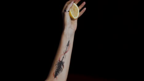 Close-up-of-female-hand-with-a-tattoo-squeezing-a-lemon-on-black-background
