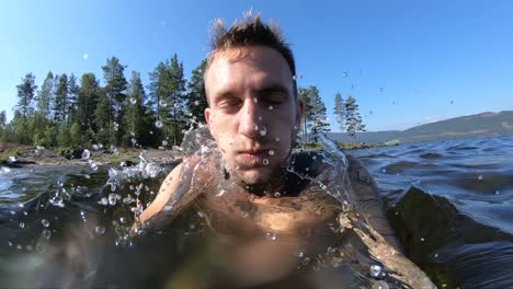 A-young-man-with-tattoos-takes-a-deep-breath-and-takes-a-dip-down-underneath-the-surface-in-the-cold-water-in-Norway-during-a-summer-vacation-trip