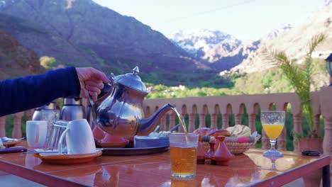 Pouring-tea-from-silver-teapot-on-rooftop-terrace,-Morocco,-slow-motion