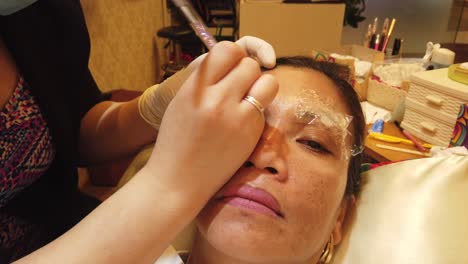 A-hand-doing-eyebrow-threading-to-a-lady-eyebrow-using-sharp-blade-and-ink
