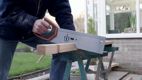 A-man-sawing-a-piece-of-wood-on-a-workbench-outside