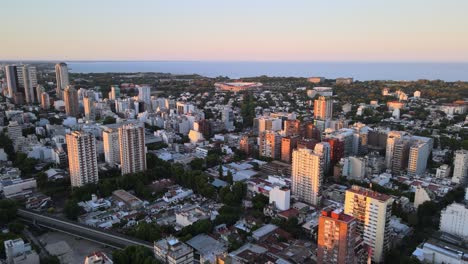 Dolly-in-flying-over-Belgrano-neighborhood-buildings-at-sunset,-Rio-de-la-Plata-river-in-background,-Buenos-Aires,-Argentina