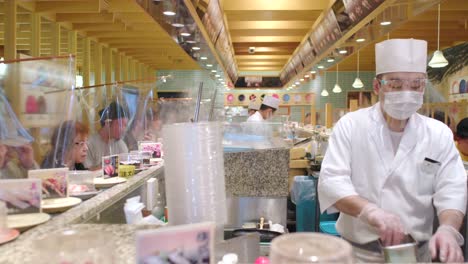 Szene-Im-Kaiten-Zushi-Restaurant-In-Tokio,-Japan,-Mit-Koch,-Der-Einen-Gesichtsschutz-Trägt,-Und-Kunden,-Die-Durch-Plastikfolienbarrieren-Getrennt-Sind,-Um-Die-Ausbreitung-Des-Coronavirus-Zu-Verhindern-–-Mittlere-Aufnahme