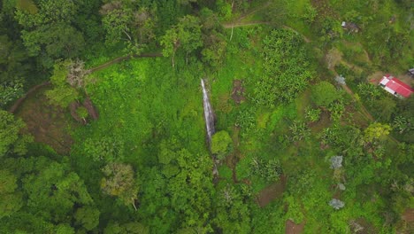 Drone-flies-towards-a-tiny-waterfall-in-the-centre-of-a-forest-covered,-mist-topped-hillside-on-a-cloudy-day