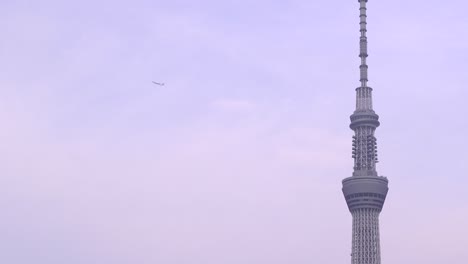 Tilt-up-shot-of-Tokyo-Skytree-and-airplane-flying-with-backdrop-of-blue-sky