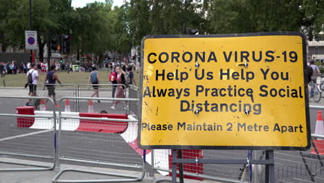 People-cross-a-pedestrian-crossing-behind-a-yellow-information-road-sign-that-says,-“Corona-Virus-19