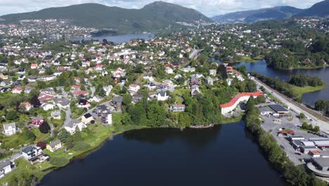 Small-Nesttun-water-with-expensive-neighborhood-and-light-rail-Bybanen-close-by---Road-to-Bergen-passing-into-background---Norway-aerial