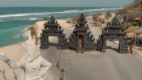 Monument-of-Hindu-God-at-entrance-gate-to-Melasti-Beach,-Bali,-Indonesia,-aerial