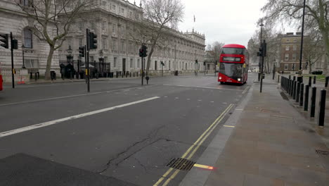 Double-decker,-red,-bus-passing-on-an-empty-White-Hall-street-right-next-to-Downing-Street-entrance