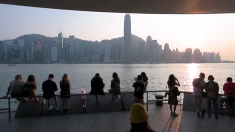 Menschen-Versammeln-Sich-Am-Ufer-Des-Victoria-Harbour-Und-Genießen-Den-Blick-Auf-Die-Skyline-Der-Insel-Hongkong,-Während-Der-Sonnenuntergang-Untergeht