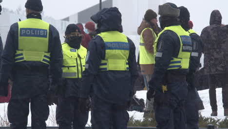 Medium-wide-shot-showing-a-group-of-armed-police-officers-on-duty-in-Helsinki-during-a-demonstration-over-Covid-19-restrictions,-cold-snowy-day