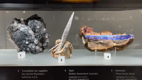 Exhibición-De-Gemas-De-Tucson:-Exhibición-De-Minerales-De-Cuarzo,-Hematita,-Corindón-Y-ópalo-En-Una-Vitrina-De-Vidrio