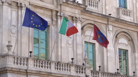 The-flags-of-European-Union,-Italy-and-University-of-Catania-waving-in-wind-on-the-building-of-the-university