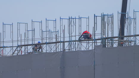 Two-Japanese-construction-workers-in-full-PPE-working-in-the-heatwave-on-top-of-a-tall-building-in-Japan
