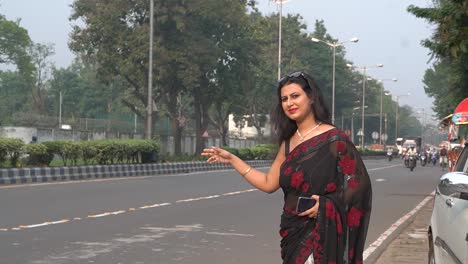 An-Indian-woman-in-black-saree-standing-in-the-highway-road-wearing-sun-glass-in-head-asking-for-lift-in-trees-background