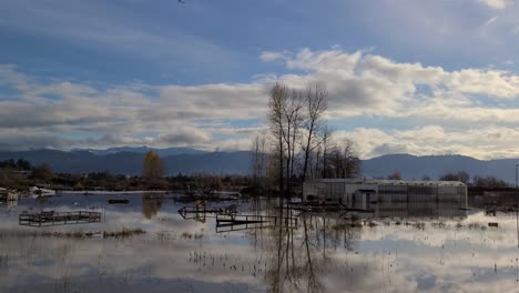 The-mirror-like-surface-of-a-flooded-farm-and-a-greenhouse-in-Abbotsford-reflects-a-blue-sky-and-some-light-clouds