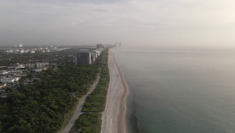 Misty-fog-sunrise-aerial-over-empty-Surfside-sand-beach,-Miami-Florida