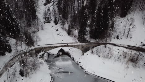 Mit-Schnee-Bedeckte-Steinbrücke-Bei-Schneefall-In-Majestätischer-Hügellandschaft,-Luftaufnahme