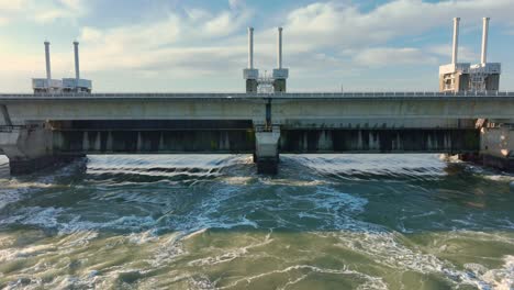 Aerial-shot-zooming-out-of-water-flowing-through-the-Eastern-Scheldt-storm-surge-barrier-in-Zeeland,-the-Netherlands,-on-a-beautiful-sunny-day