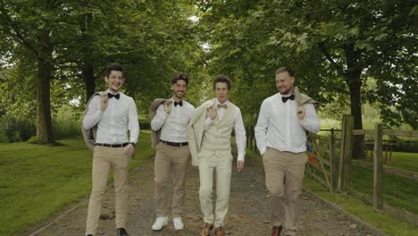 GROOM-WITH-GENTLEMEN-WALKING-TOGETHER-IN-THE-WOODS-TO-THE-CEREMONY,-BEAUTIFUL-COUNTRYSIDE-AROUND-AND-THEY-WALK-SMILING-TO-THE-GROOM-IN-A-BEAUTIFUL-DECOR