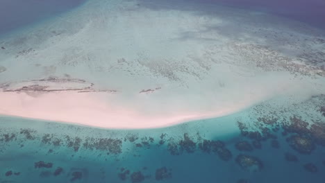 Rotating-high-sea-aerial-of-small-sand-islet-dotted-with-coral-reefs