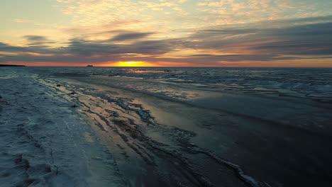 A-fast-flight-over-a-winter-beach-and-a-frozen-sea-on-sunset