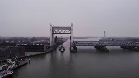 En-Avant-9-Schleppkahn,-Der-Schweres-Gerät-über-Den-Fluss-Transportiert-Und-Dabei-Eine-Offene-Eisenbahnbrücke-In-Dordrecht,-Niederlande,-Passiert