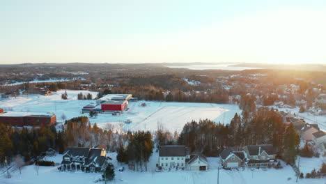 Scenic-winter-aerial-flying-over-snow-covered-homes-and-a-school-field-at-sunset