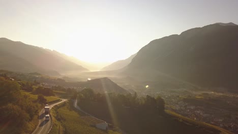 Drohnenaufnahme-Am-Frühen-Morgen,-Als-Die-Sonne-über-Einem-Wunderschönen-Bergtal-Mit-Etwas-Verkehr-Auf-Der-Straße-In-Lavaux-Oron,-Schweiz,-In-4k-Aufging
