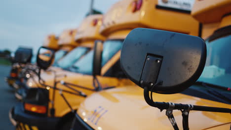 A-number-of-school-buses-to-transport-schoolchildren.-Close-up-of-car-parts-and-rear-row-of-other-vehicles