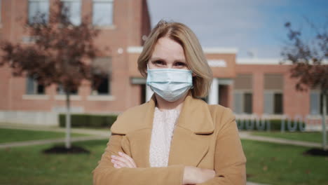 Portrait-of-a-masked-teacher-in-front-of-a-school-building-in-the-USA