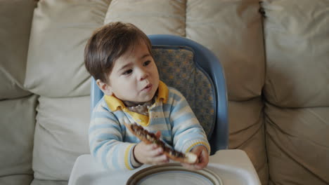 Asian-baby-eats-pizza,-sits-on-the-baby's-feeding-table