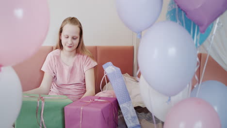 The-girl-received-many-birthday-gifts,-sits-on-the-bed-near-beautiful-boxes,-next-to-balloons