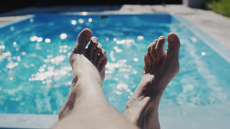 A-man-is-relaxing-by-his-pool,-legs-are-visible-in-the-frame